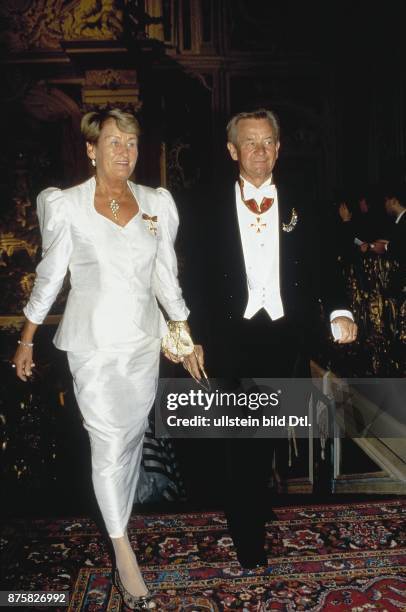Der deutsche Verleger Gustav Heinrich Lübbe, im Abendanzug, geht neben seiner Frau Ursula, die ein weißes, glänzendes Kleid trägt. Beide tragen einen...
