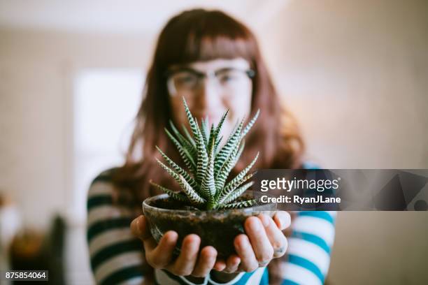 Young Adult Woman At Home Showing Her Plant