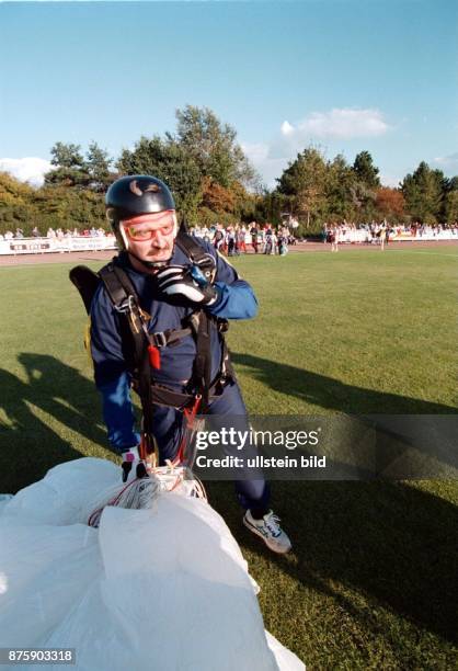 Der Politiker Jürgen Möllemann steht nach einem Fallschirmsprung auf der Rasenfläche eines Sportplatzes. Im Hintergrund sind Zuschauer zu erkennnen. .