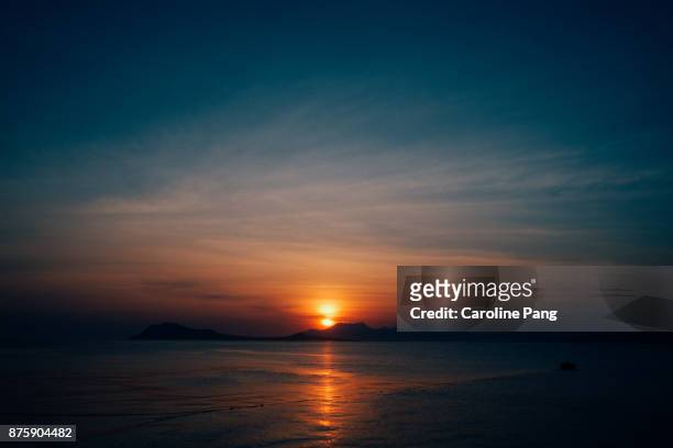 sun sets behind the mountains as seen from the coast of ende, flores, indonesia. - caroline pang stock-fotos und bilder