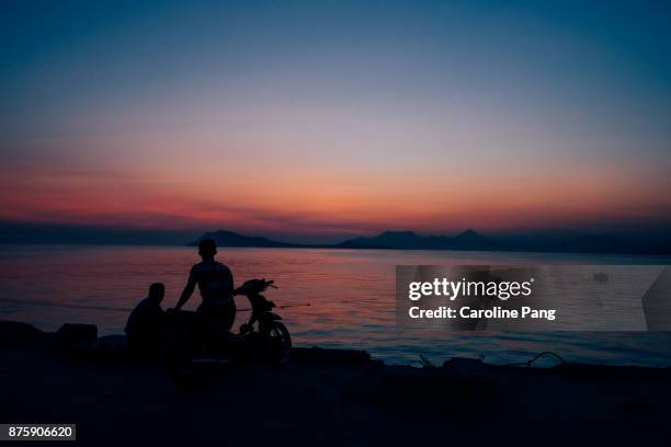 people indulging in the moment of sunset at the port of ende. - caroline pang stockfoto's en -beelden