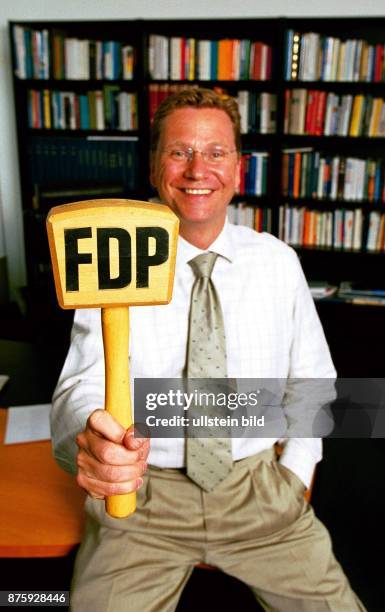 Der FDP-Generalsekretär Guido Westerwelle sitzt in seinem Büro und hält einen gelben Holzhammer mit dem Schriftzug FDP in der Hand. .