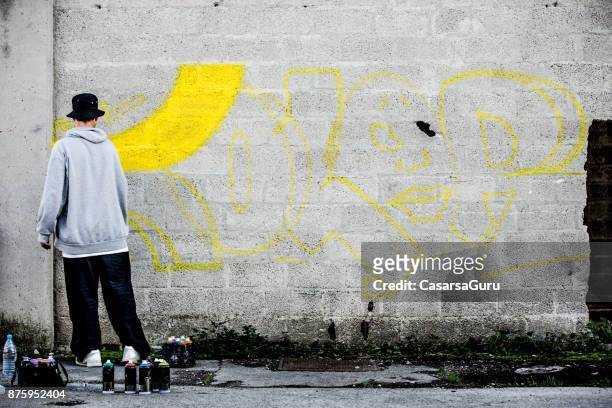 late teen graffiti artist drawing graffiti on wall - graffiti text stock pictures, royalty-free photos & images