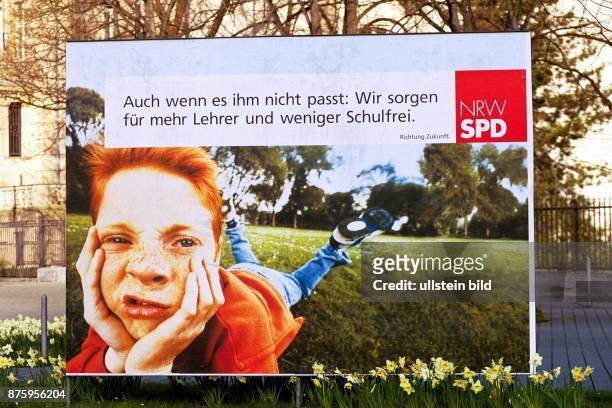 Ein rothaariger Junge mit Sommersprosssen liegt bäuchlings auf einer Wiese und zieht ein Gesicht. Ein Wahlplakat der SPD für die...