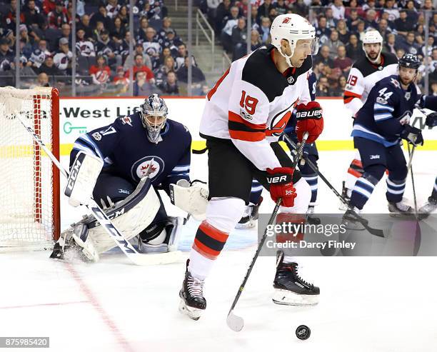 Goaltender Connor Hellebuyck of the Winnipeg Jets watches as Travis Zajac of the New Jersey Devils plays the puck during third period action at the...