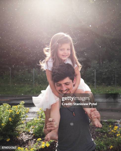 Father with daughter on shoulders having fun , rain and sun