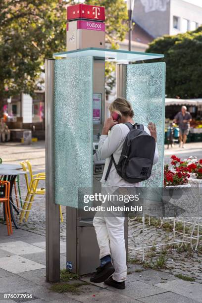 Deutschland Germany Berlin Frau telefoniert an einer Telefonzelle mit gesplittertem Glas in Berlin-Spandau.