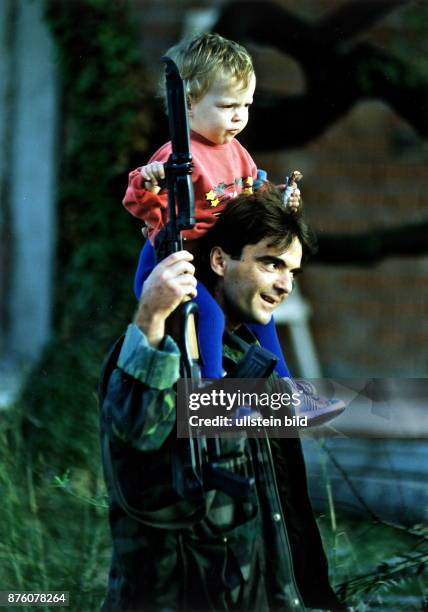 Ein kroatischer Soldat mit seiner Kalaschnikow und aufgesetztem Bajonett trägt seine Tochter auf den Schultern. November 1991