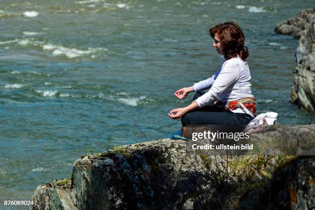 Eine Frau meditiert auf einer Klippe unweit des Zusammenflusses der Flüsse Katun und Chemal. 1.5.2016, mittags, Chemal, Republik Altai, Russland.