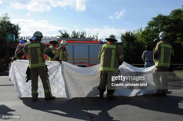 Feuerwehrmänner schützen ein Unfallopfer mit einer Decke vor neugierigen Blicken