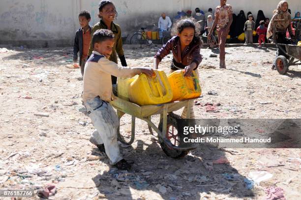 Children help their older sister to move a wheelbarrow carrying jerry cans after they collected clean water from a charity water pipe on November 18,...