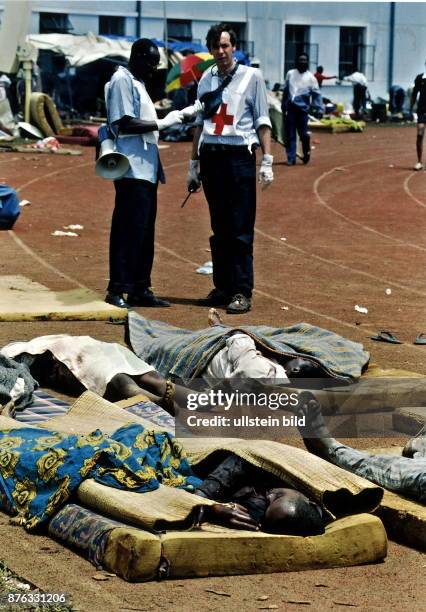 Fussballstadion Kigali: Tutsi Opfer eines Granatangriffs auf Matratzen. Im Hintergrund Helfer des Roten Kreuz Mai 1994