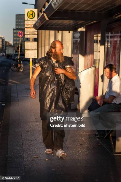 Deutschland Germany Berlin Obdachloser mit Plastiksack und mit Plastik verbundenen Füssen an einer Bushaltestelle am Potsdamer Platz.