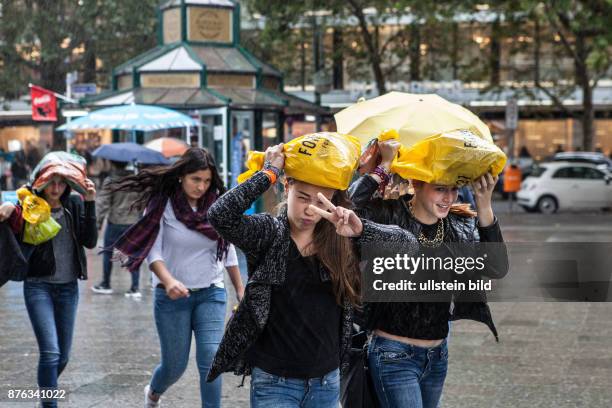 Deutschland Germany Berlin Junge Frauen laufen, ihre Einkaufstüten als Schutz über dem Kopf, durch den Regen.