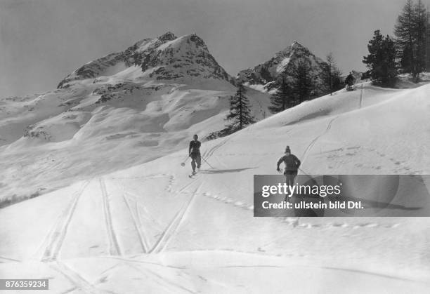 Two skiers take the descent in a snowy winter landscape in the high mountains of the Swiss Alps Vintage property of ullstein bild