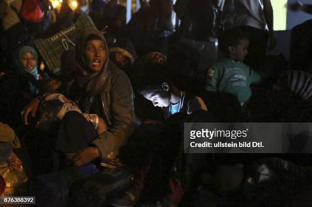 Flüchtlinge warten am Hafen von Kalymnos auf die Fähre nach Athen, Flüchtlingskind sitzt in der Menge mit einem Smartphone das sein Gesicht...