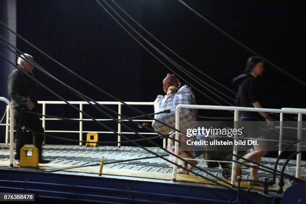 Flüchtlingsfrau mit Kopftuch geht schwer bepackt auf die Fähre in Richtung Athen, Nachtaufnahme, weitere Fahrgäste sind zu sehen