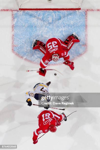 Jimmy Howard of the Detroit Red Wings makes a save behind teammate Xavier Ouellet and Benoit Pouliot of the Buffalo Sabres during an NHL game at...