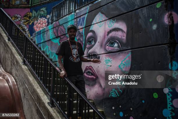 Man stands in front of a graffiti, portraying a young girl staring at the sky, in Medellin, Colombia on November 19, 2017. Mural graffitis from...