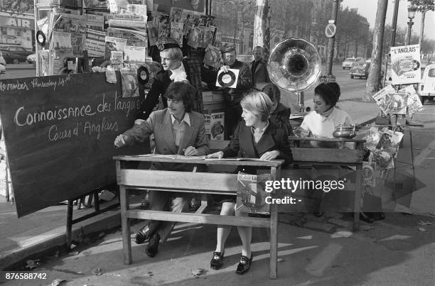 Le chanteur Antoine est assis à un pupitre d'école à l'occasion du lancement d'une nouvelle méthode de langues vivantes sur l'avenue des champs...