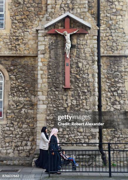 Two Muslim women and a child pass a Christian church and Crucifix in London, England.