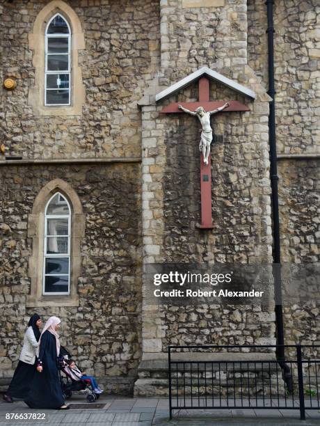 Two Muslim women and a child pass a Christian church and Crucifix in London, England.