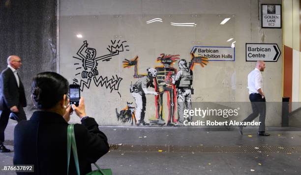 Woman photographs street art created in September 2017 near the Barbican Centre in London, England, by Banksy, an anonymous England-based graffiti...
