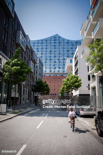 a woman rides a bike through a hafen city street towards the elbe philharmonic hall, in spring - konzerthaus stock-fotos und bilder