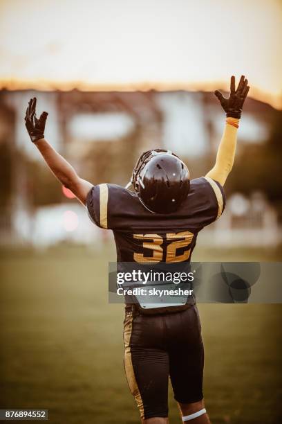 rear view of american football player standing on the field with raised arms. - american football player back stock pictures, royalty-free photos & images