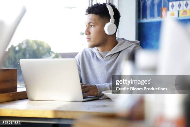 young man wearing headphones using a laptop - hoodie headphones - fotografias e filmes do acervo