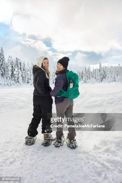 millenial young women snowshoeing across frozen lake in snowy forest - snowshoeing stock pictures, royalty-free photos & images