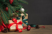 Christmas holiday background. Gifts with a red ribbon, Santa's hat and decor under a Christmas tree on a wooden board.