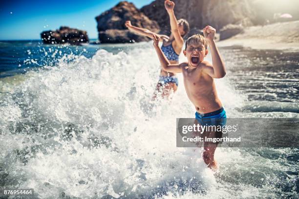 kinderen met plezier in enorme golven op het strand - droplet sea summer stockfoto's en -beelden