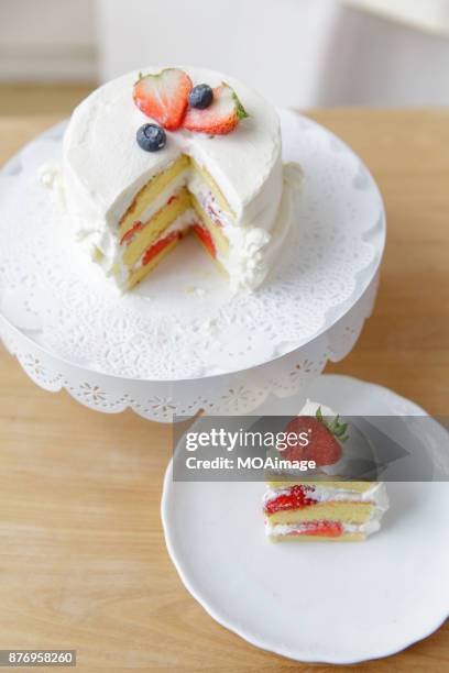 a white cream fruit cake on a cake stand is put on a wooden table - backstand stock-fotos und bilder
