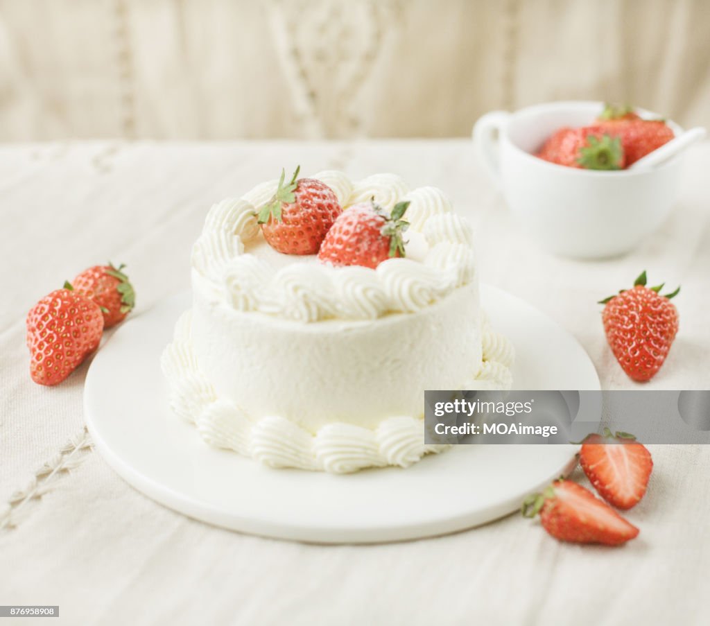A strawberry cream cake on a white plate is put on a wooden table
