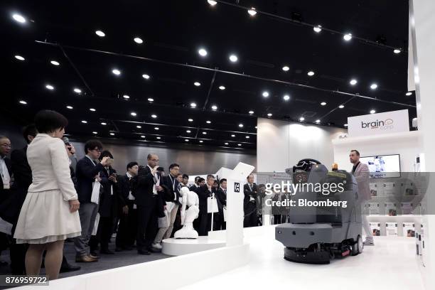 Attendees look at an International Cleaning Equipment RS26 rider auto scrubber, powered by Brain Corp.'s Brain OS, during a demonstration at the...