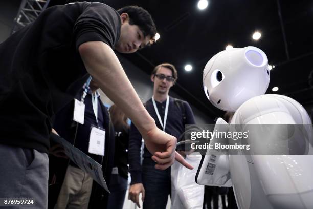 An attendant, left, demonstrates an application on a SoftBank Group Corp. Pepper humanoid robot at the SoftBank Robot World 2017 in Tokyo, Japan, on...