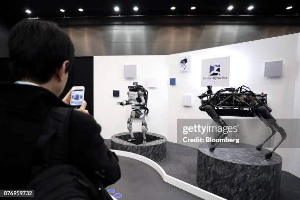 An attendee uses his smartphone to take a photograph of a Boston Dynamics Inc. Atlas humanoid robot, left, and Spot robot displayed at the SoftBank...