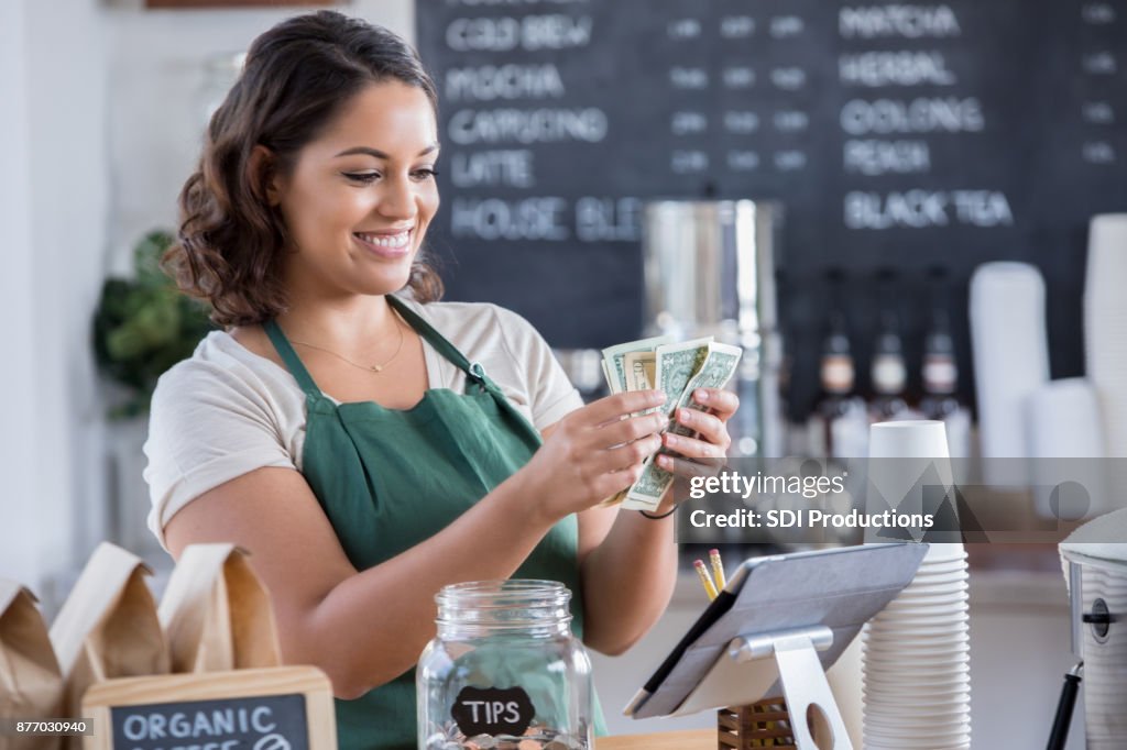 Junge weibliche Barista zählt Geld aus Glas Tipps