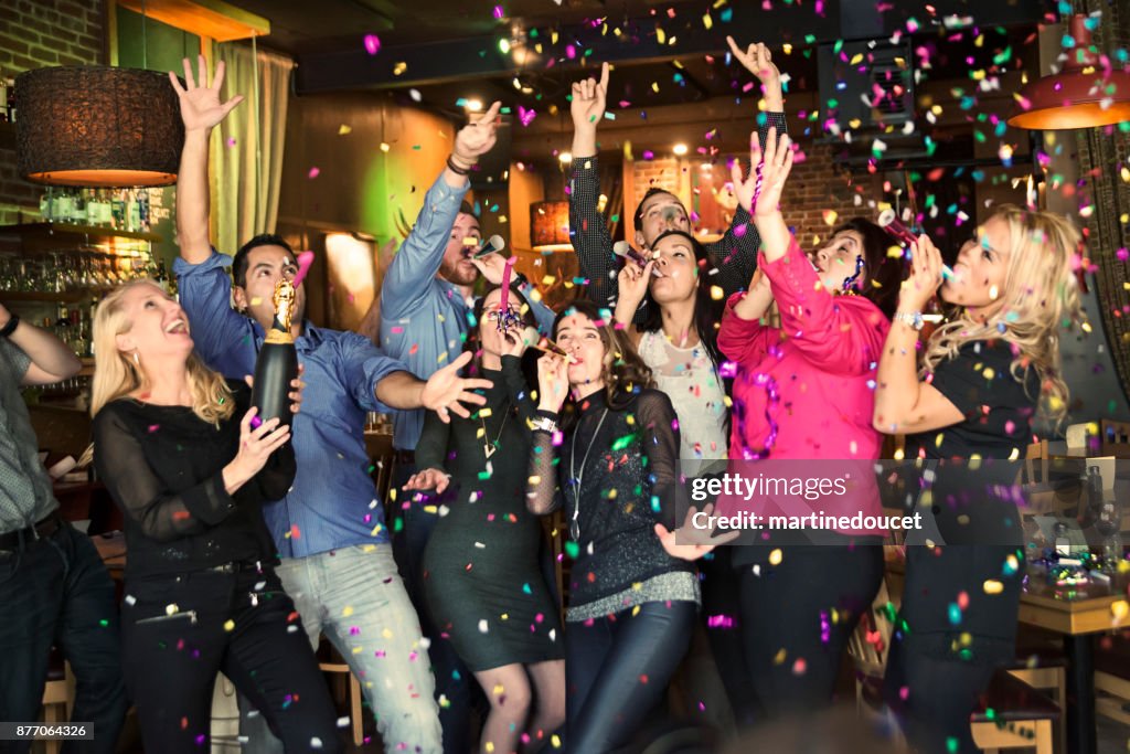 Friends and coworkers celebrating with confettis  in a bar.