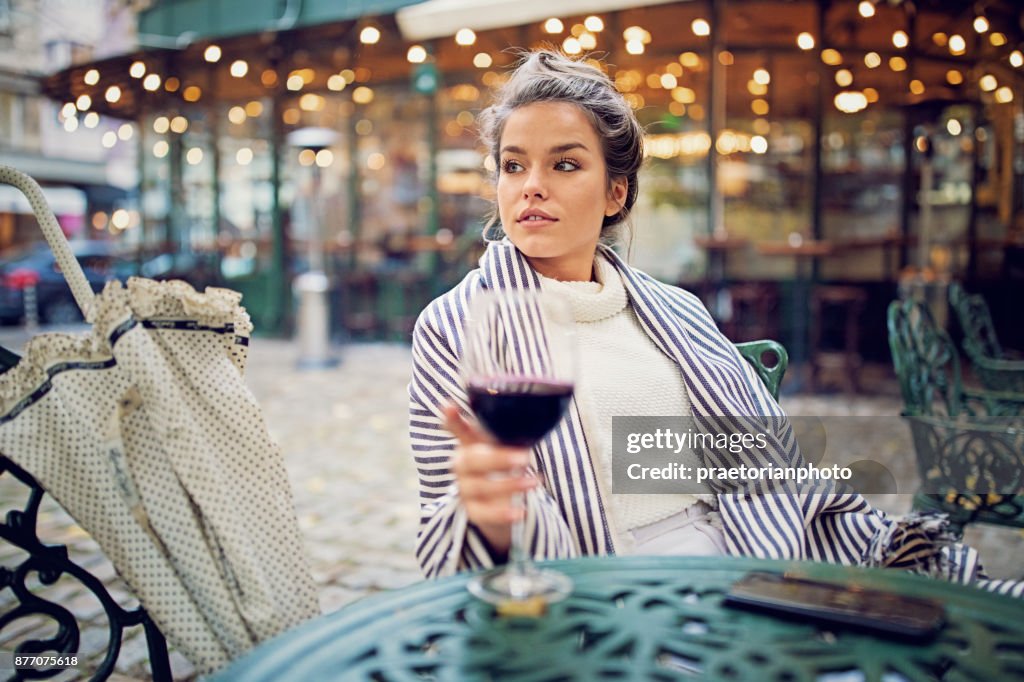 Jeune femme boit du vin à l’avant de la cafétéria dans un jour de pluie