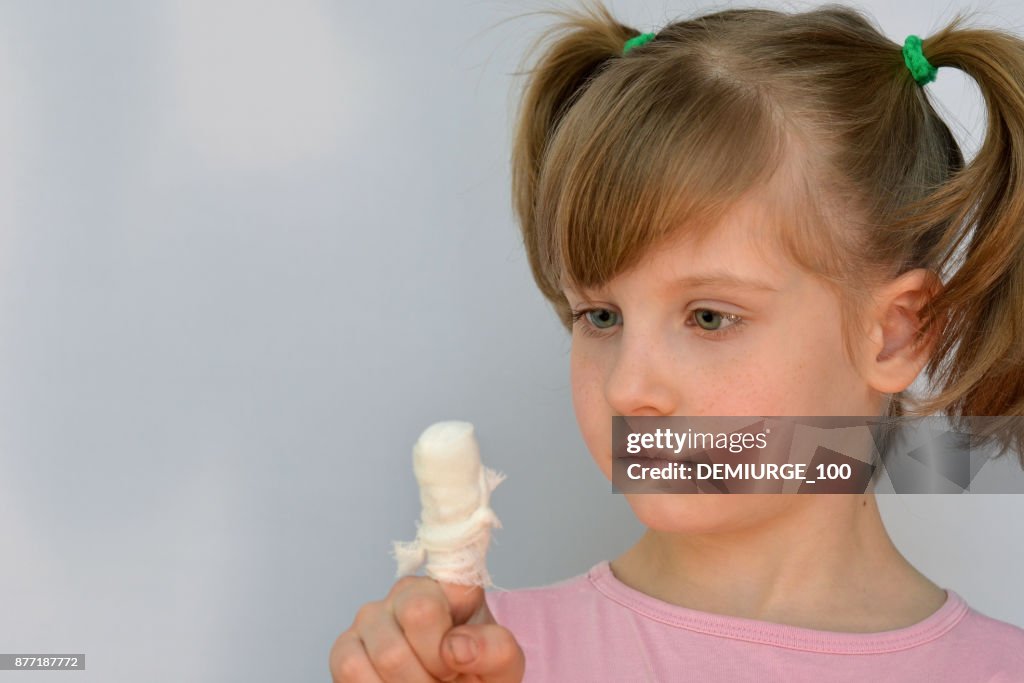 Child looks at his bandaged finger.Childhood traumas.Portrait of a little girl on a light background.