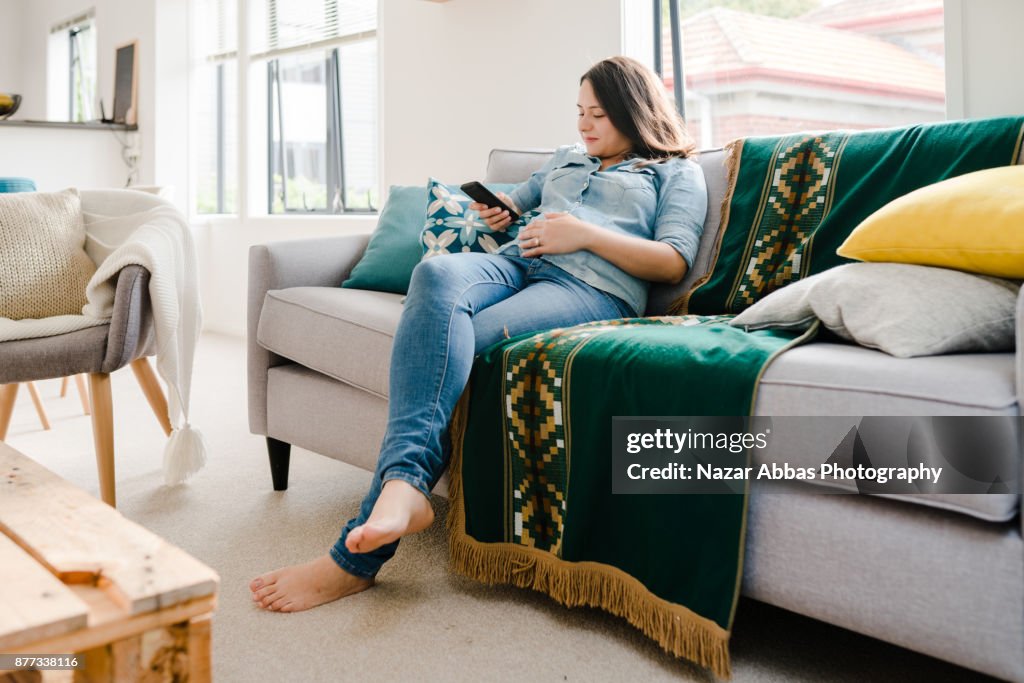 Pregnant woman relaxing at home with smartphone in her hand.