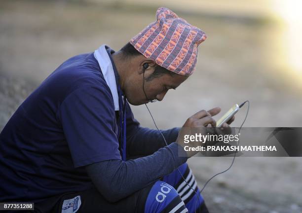This photograph taken on November 18, 2017 shows A Nepali man listening to the radio with his mobile phones in Dhankuta, some 400 km east of...