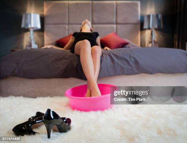 young woman lying on bed wth feet resting in tub of warm water. - wash bowl stockfoto's en -beelden