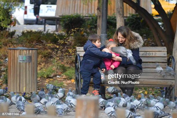 Woman and two children feed pigeons at the Kugulu Park during a cold autumn day in Ankara, Turkey on November 22, 2017.