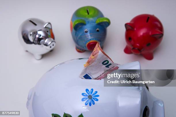 Symbol photo on the topic of saving money. The photo shows differend colored piggy banks and a ten euro banknote.