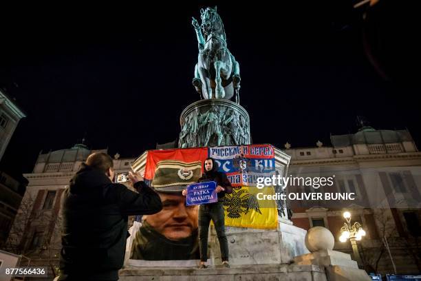 Man poses for photographs in front of the statue of Prince of Serbia Mihailo Obrenovic and a flag depicting Ratko Mladic, as he holds a placard...