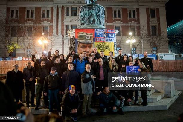 People pose for photographs in front of the statue of Prince of Serbia Mihailo Obrenovic and a flag depicting Ratko Mladic, as they hold placards...