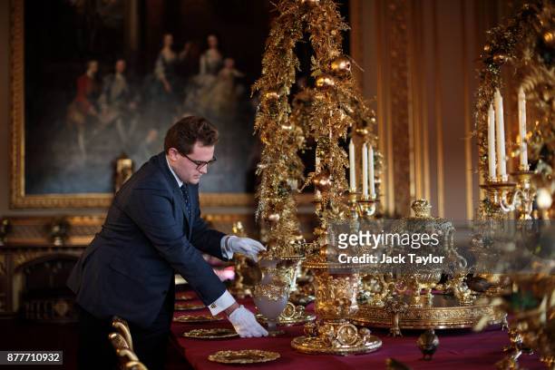 An employee poses by the table in the State Dining Room which has been decorated for the Christmas period with silver-gilt pieces from the Grand...